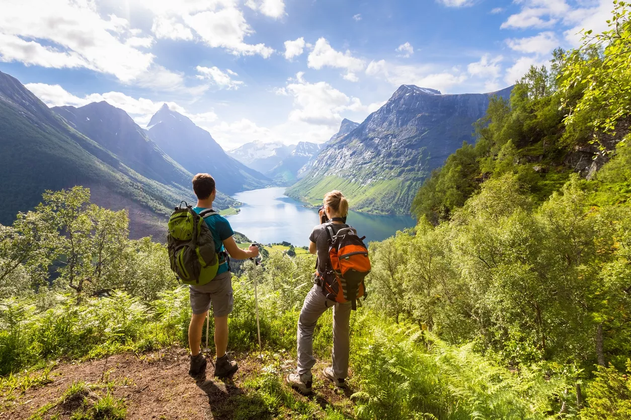 Two hikers at viewpoint in mountains with lake, sunny summer